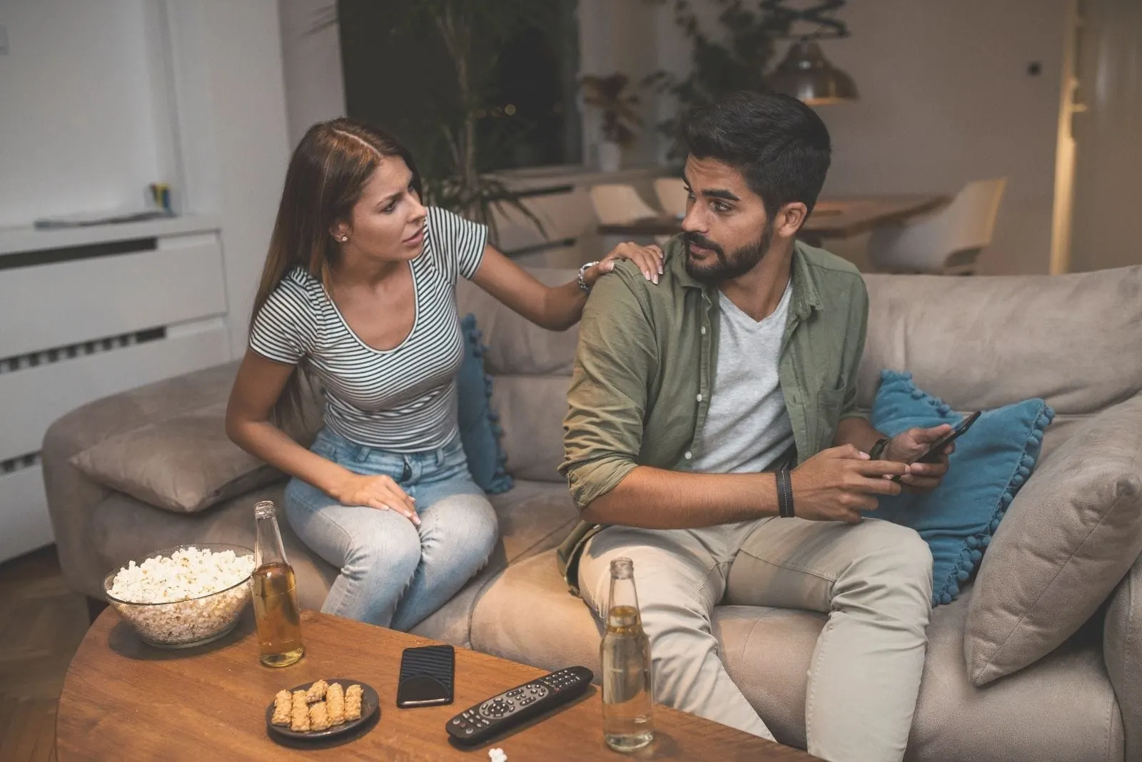 couple arguing over phone while drinking beer in their livingroom