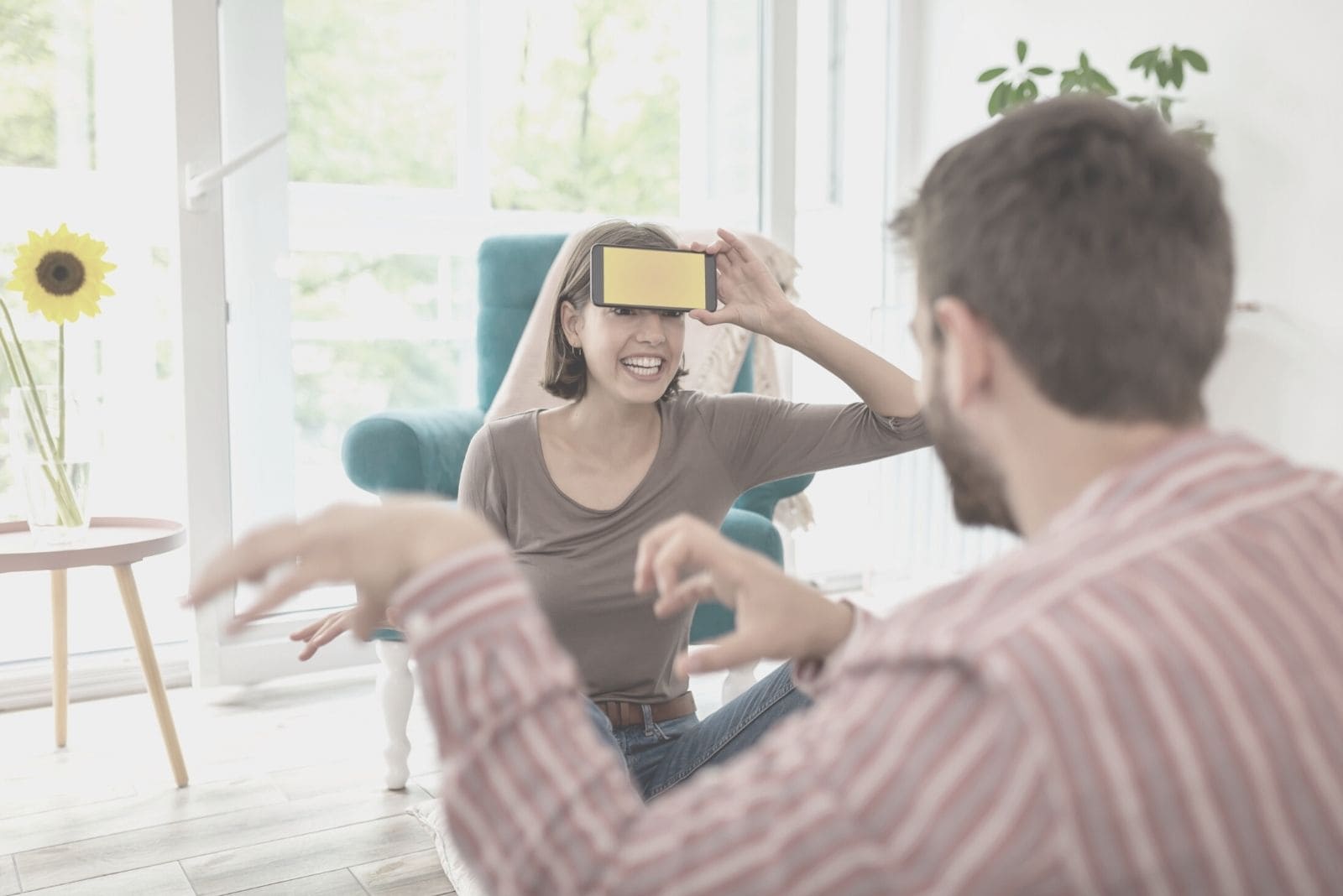 pareja divirtiendose jugando a la farsa con la mujer adivinando y sentada en el suelo del salon