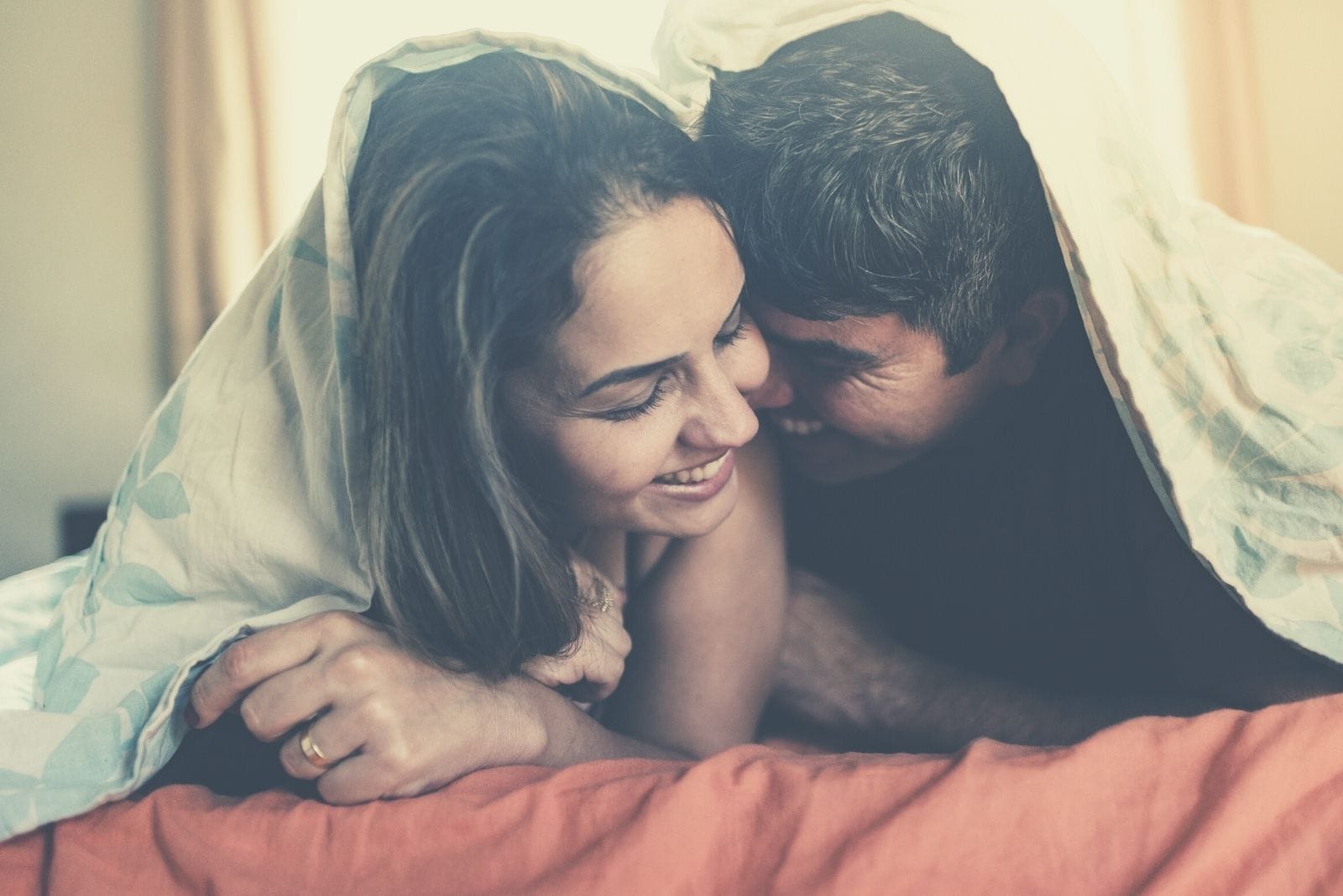 couple in the morning cuddling and happy while covered with blanket while lying in bed