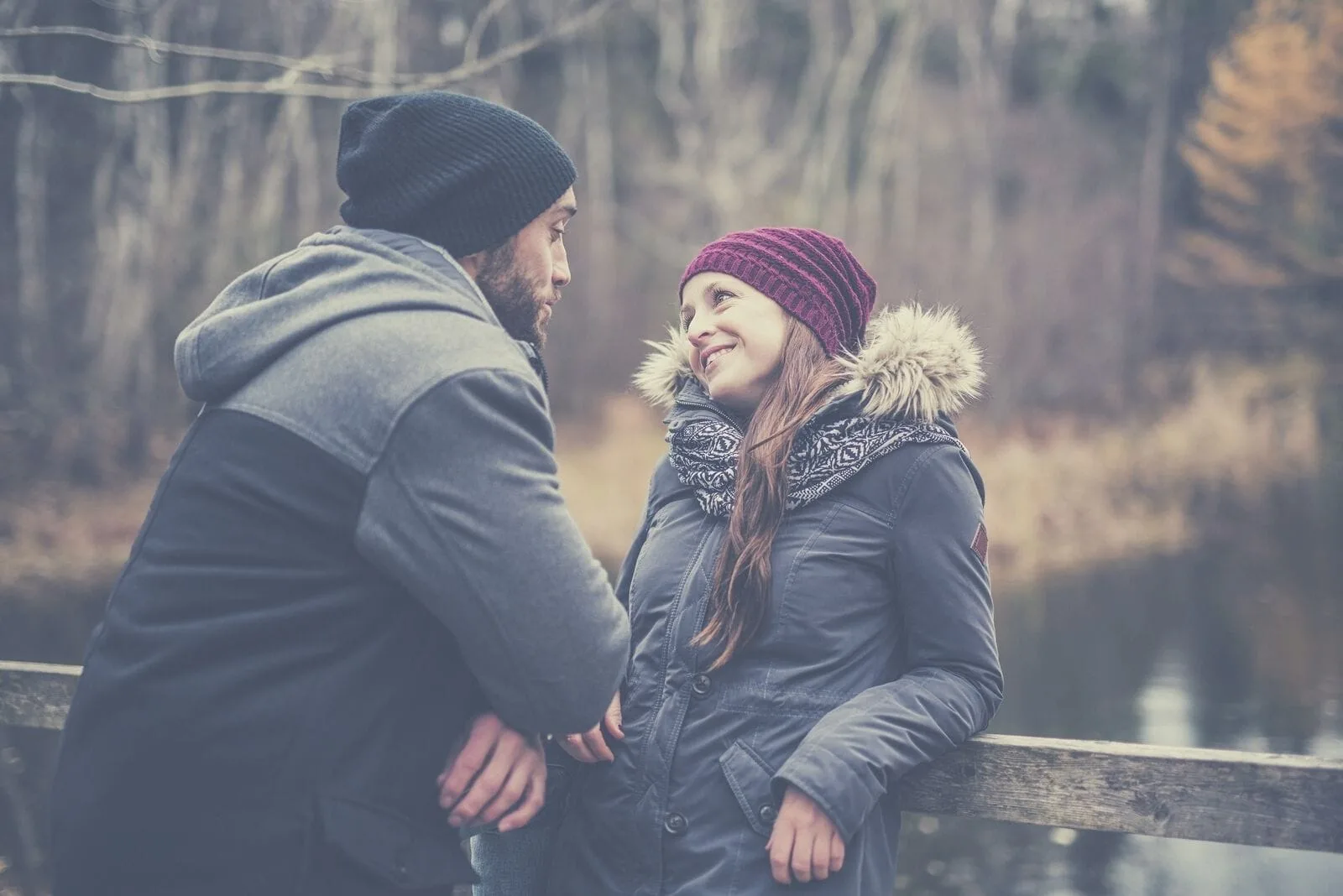 couple in winter clothes talking near the pond woman leaning on the wooden railings