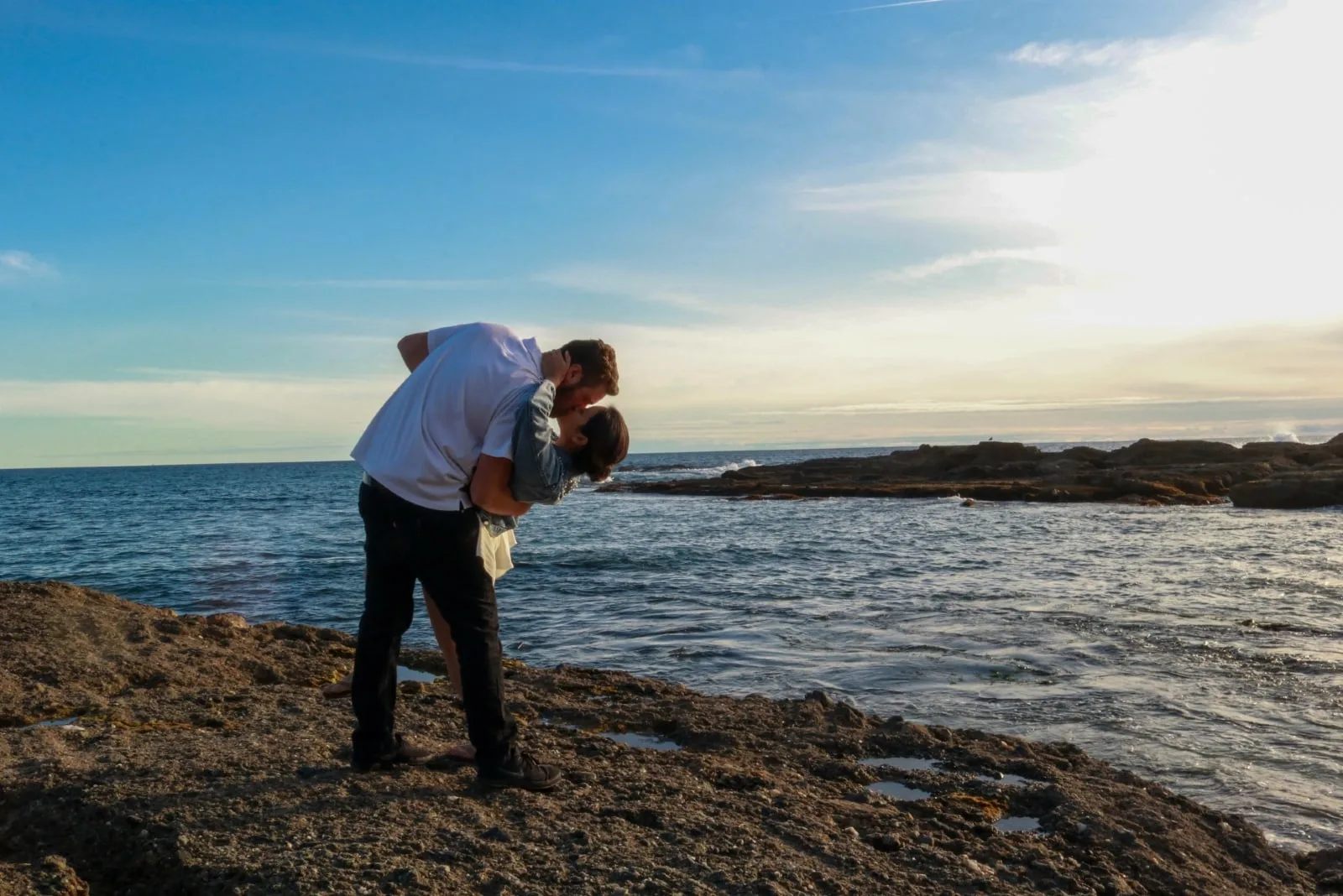 man and woman kissing while standing near sea