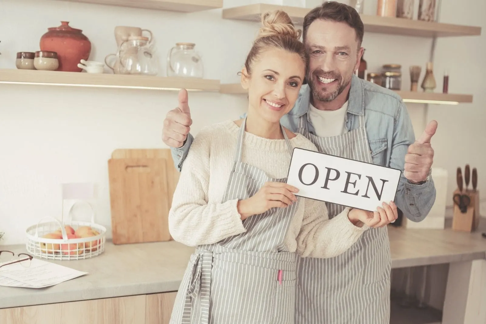 couple openning a business holding the word open wearing apron