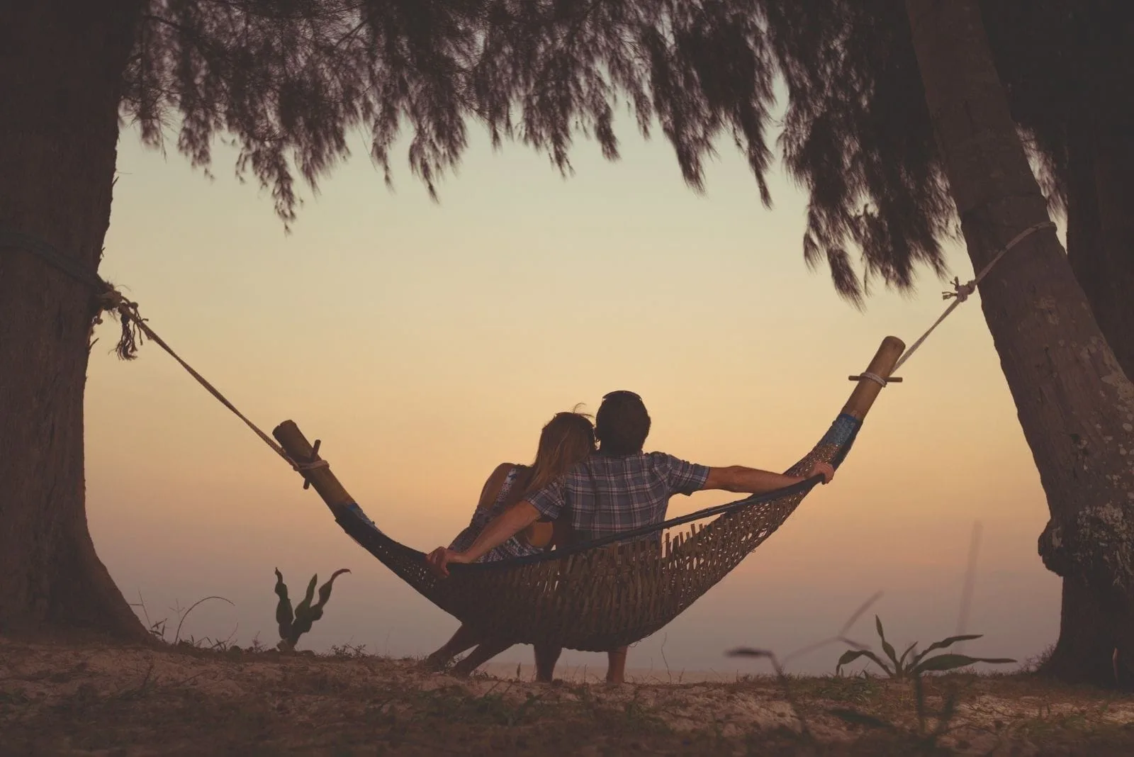 couple relaxing in a hammock hanged on trees facing the clouds on golden hour