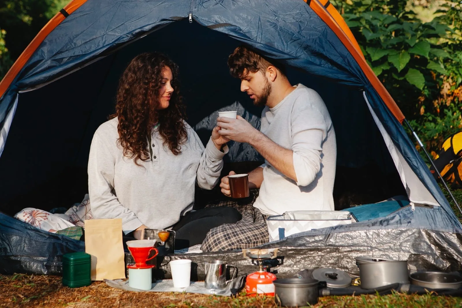 man and woman having coffee while sitting in tent