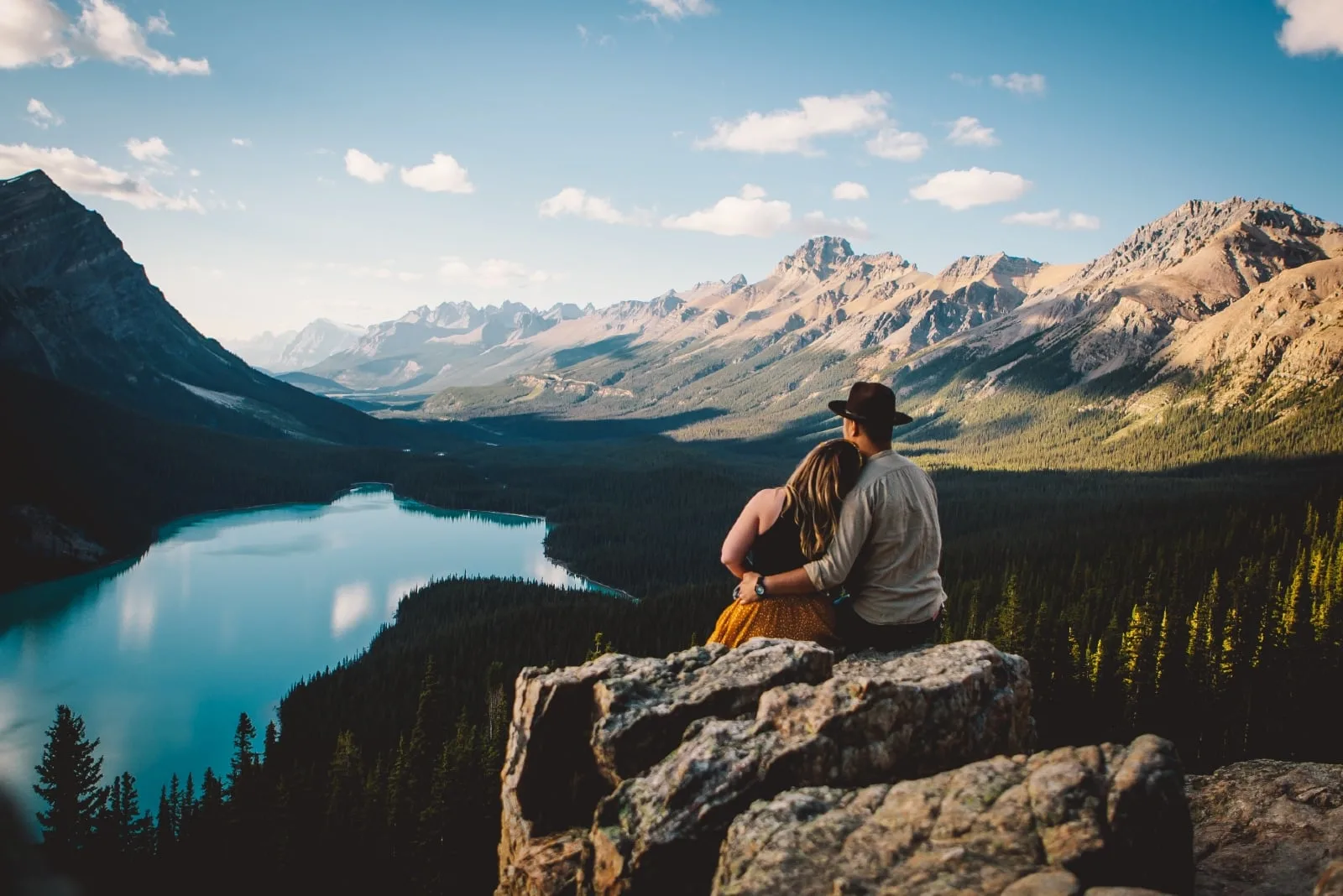 man and woman looking at lake while sitting on rock