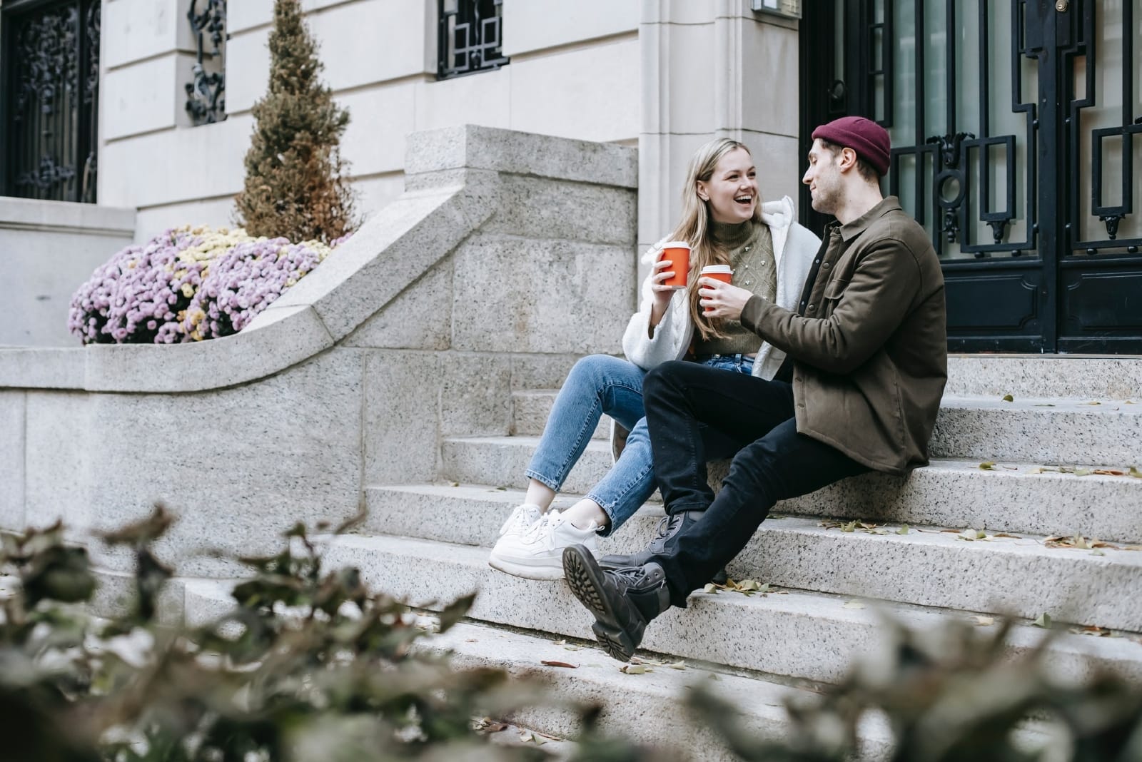 man and woman having coffee while sitting on stairs