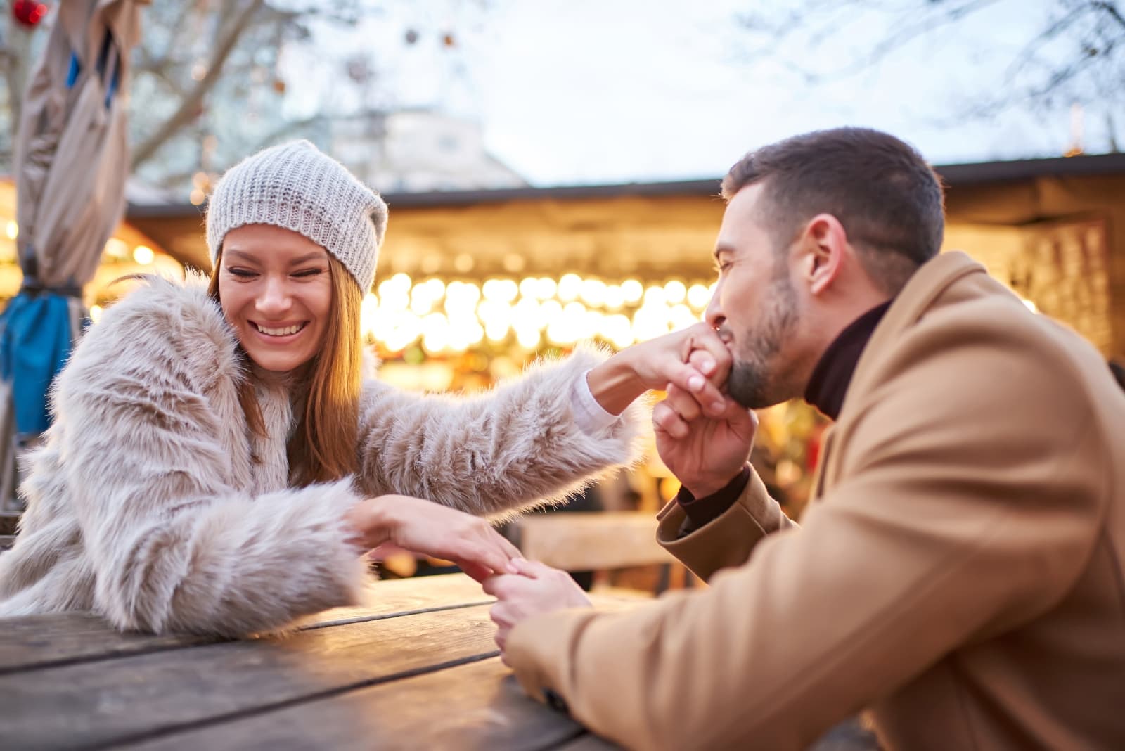 hombre feliz besando la mano de la mujer mientras se está sentado al aire libre