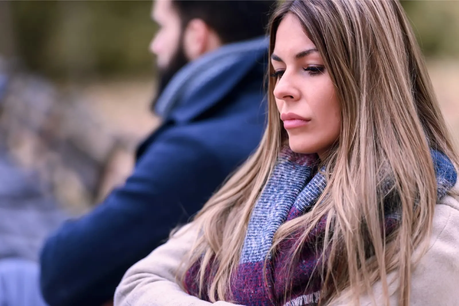 sad woman with scarf sitting near man outdoor