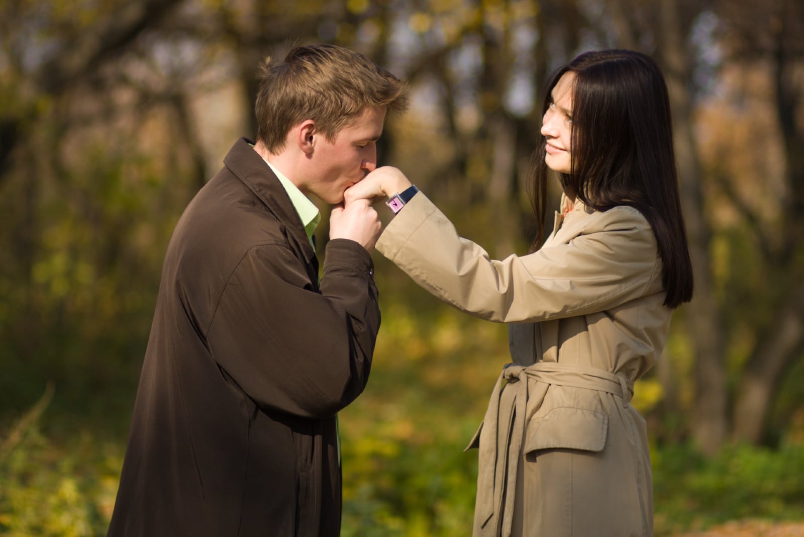 hombre con abrigo marrón besando la mano de una mujer al aire libre