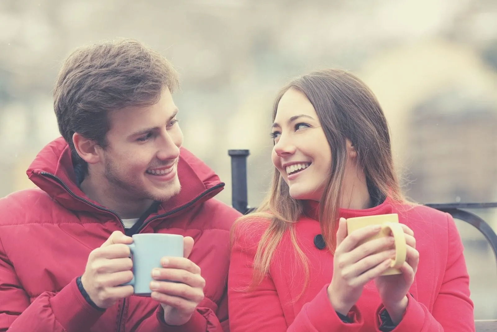 couple wearing red winter suit sitting next to each other and drinking hot beverage