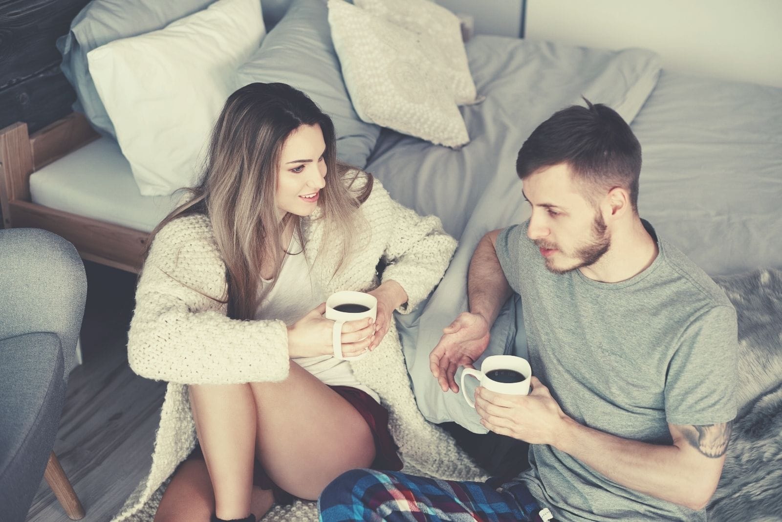 couple with morning coffee and squatting on the side of the bed while talking