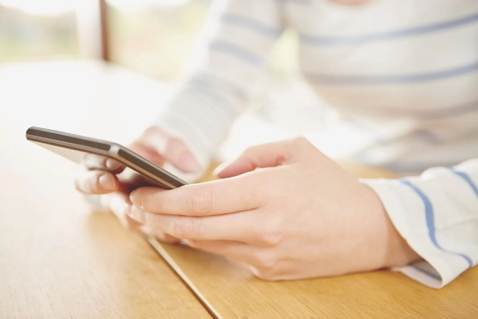 cropped image of a woman texting on a smartphone on the table
