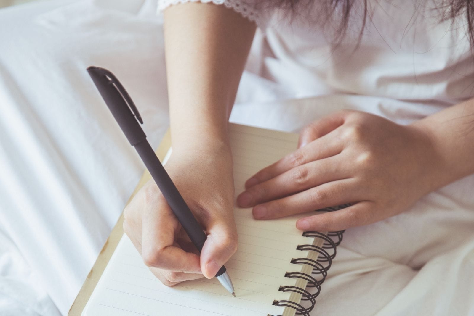 cropped photography of a woman writing down on her notebook in bed 