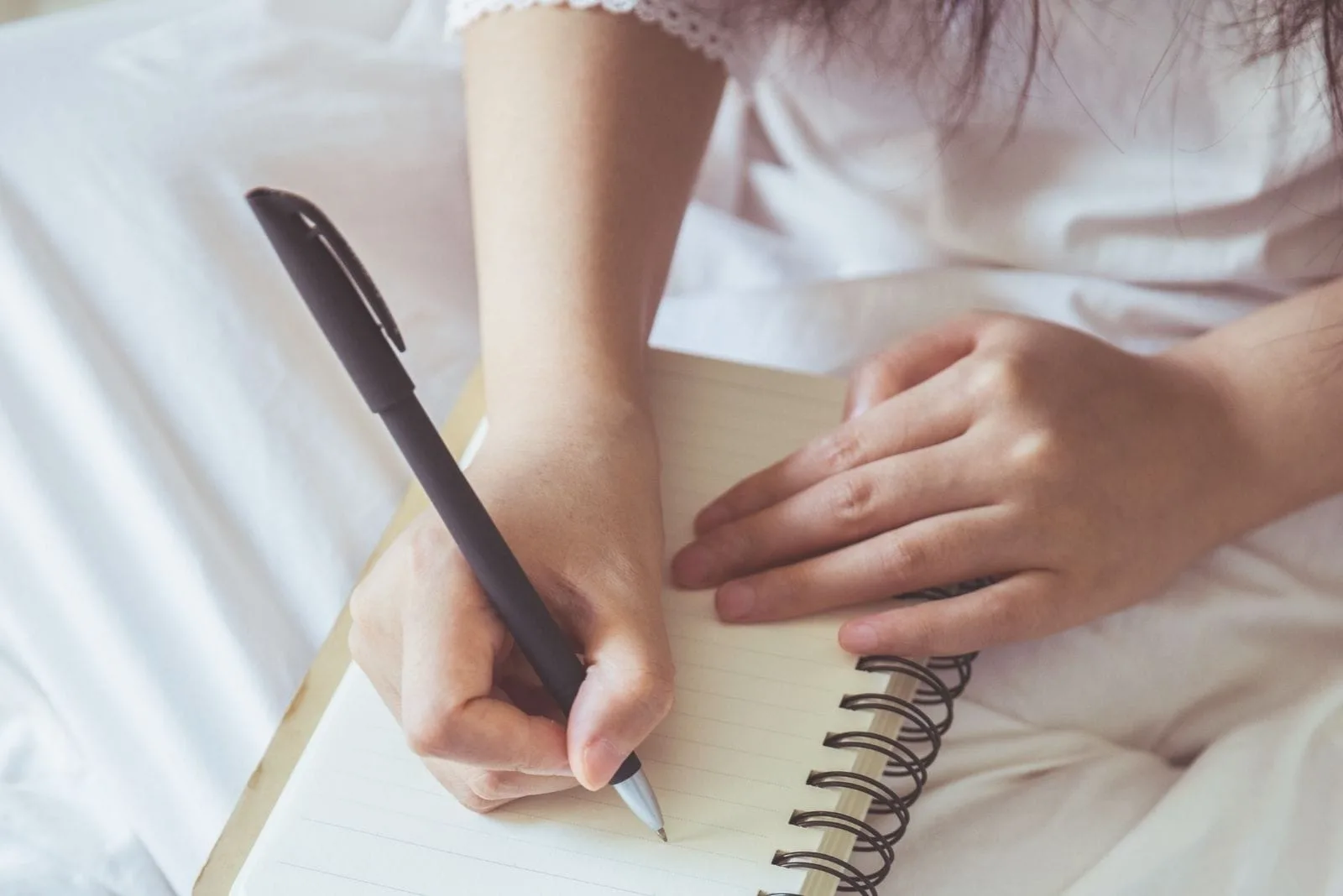 cropped photography of a woman writing down on her notebook in bed 