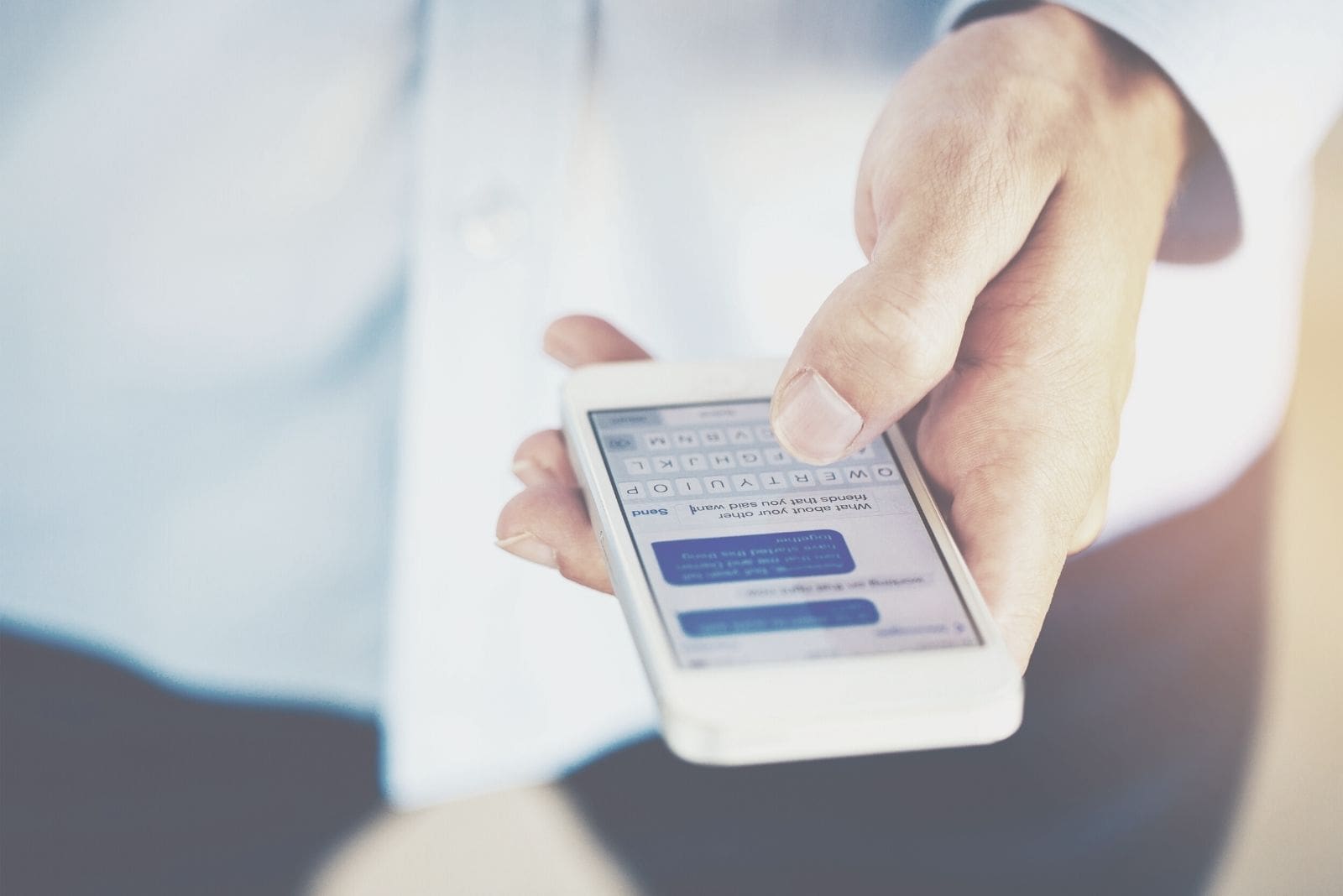 fotografia a fuoco della mano di un uomo che tiene in mano un telefono e manda un SMS