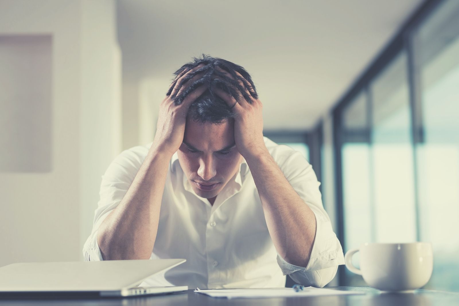 frustrato dal problema uomo che lavora nel suo computer portatile all'interno dell'ufficio con le mani in testa