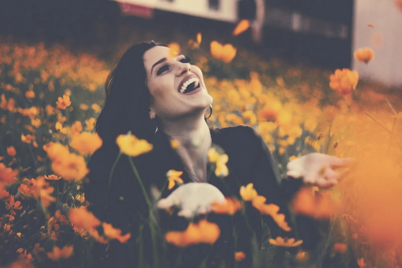 happy woman in flower field playing with orange petal flowers