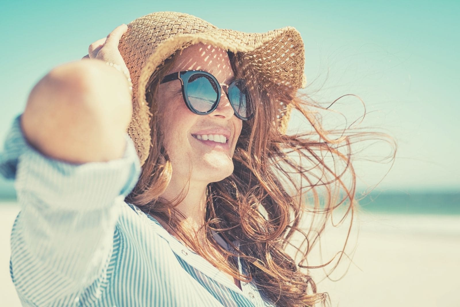 donna felice in spiaggia che sorride indossando un cappello e occhiali da vista