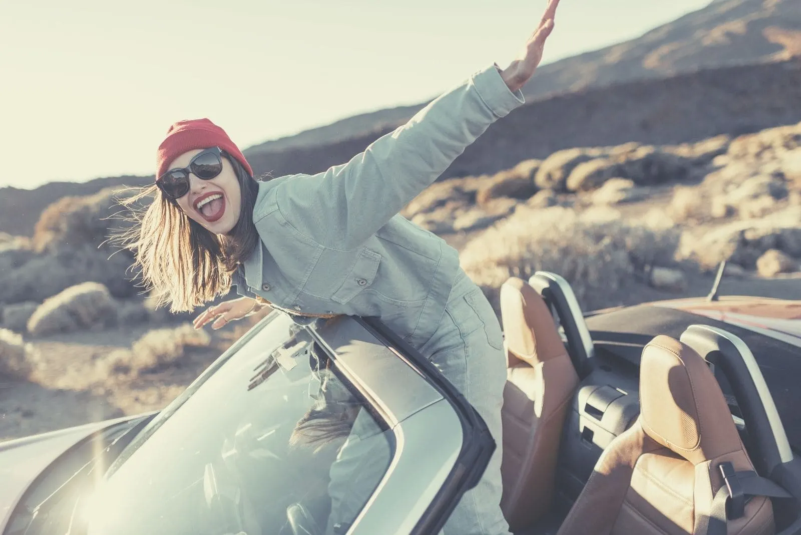 happy woman travelling by an open top down car standing on the seat