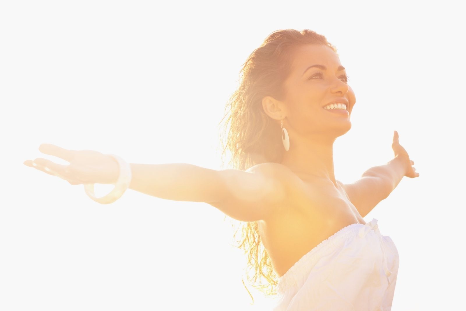 happy young woman standing with arms outstretched against sunlight in summer