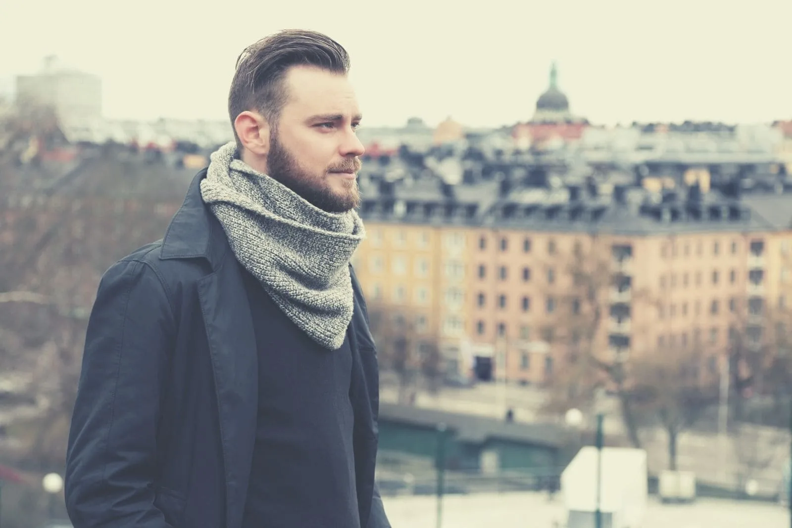 lonely pensive man with a grey scarf standing with the city behind