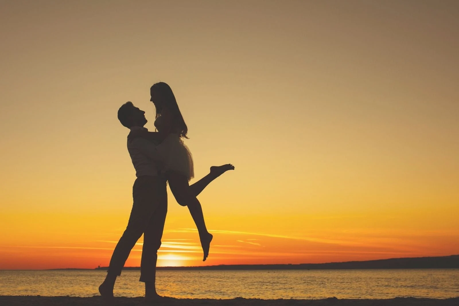 lovely couple in love silhouette during sunrise near a body of water