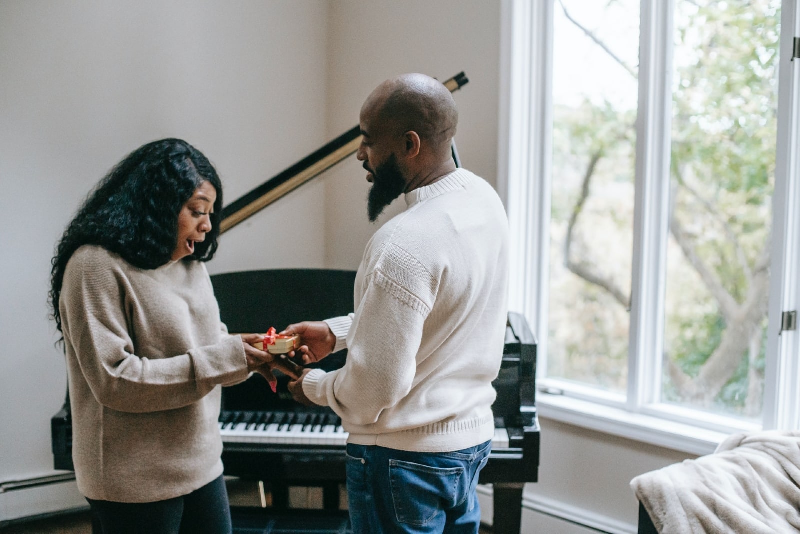man giving gift to woman while standing near piano