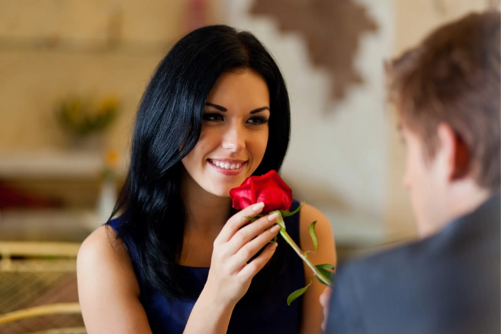man giving red rose to woman while sitting at table