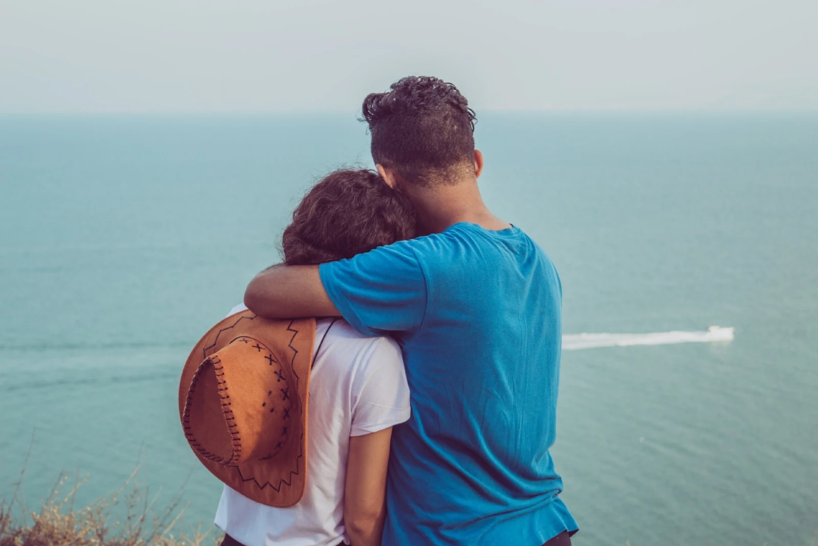 man in blue t-shirt hugging woman while looking at sea