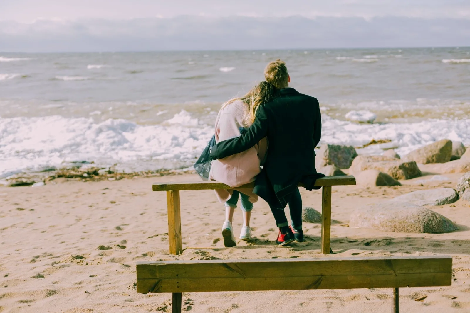 man hugging woman while looking at sea