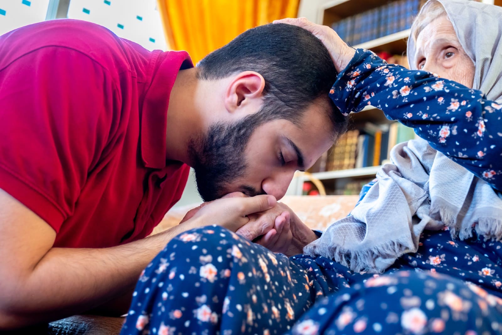 arabic muslim man in red t-shirt kissing grandmother's hand