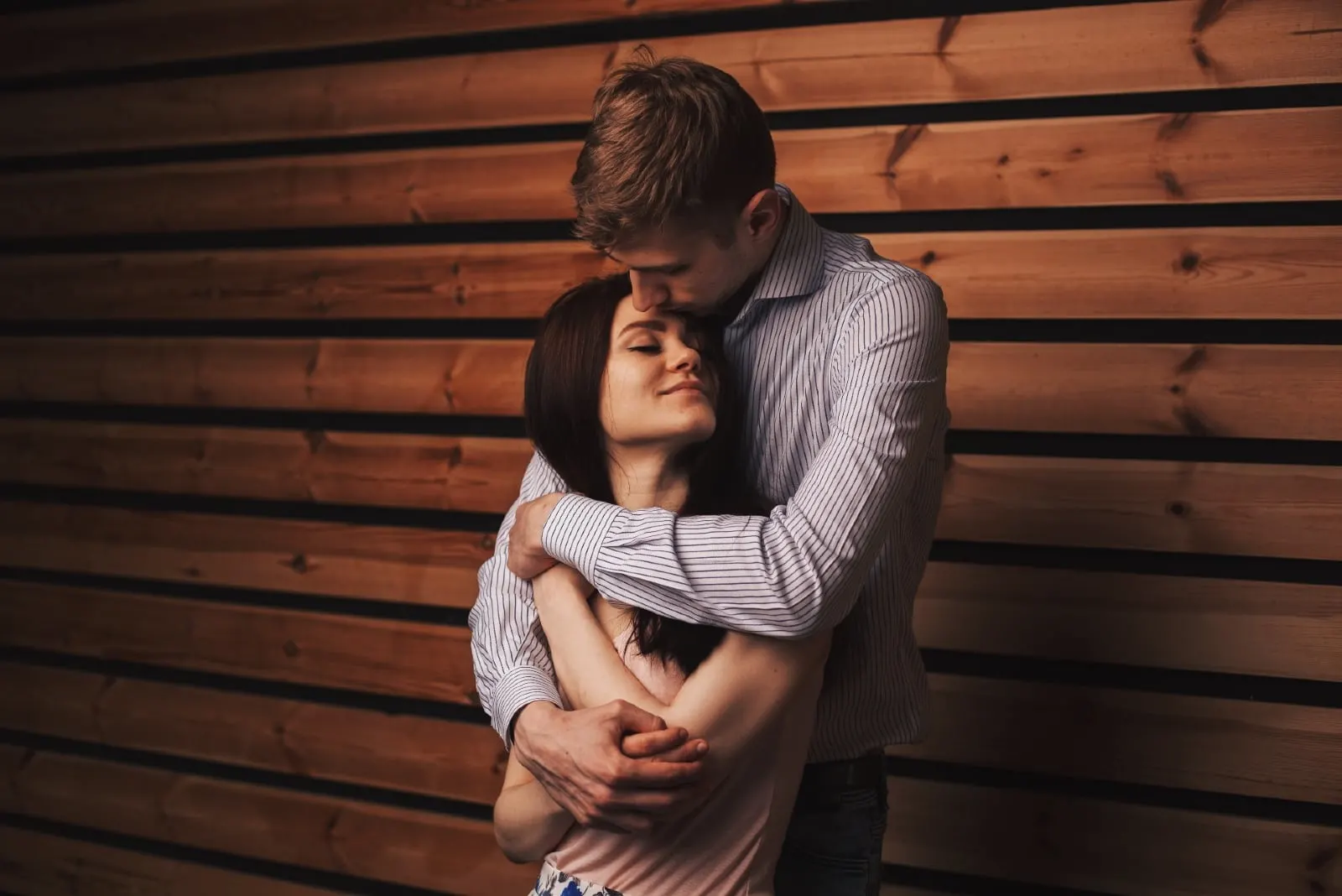 man kissing woman's forehead while standing near wooden wall