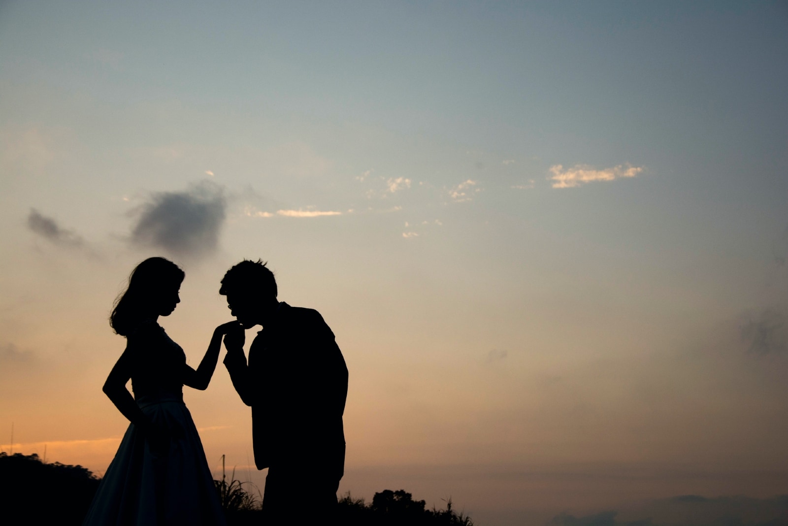 uomo che bacia la mano della donna durante il tramonto