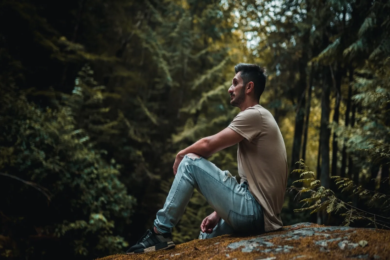 pensive man sitting on ground in forest