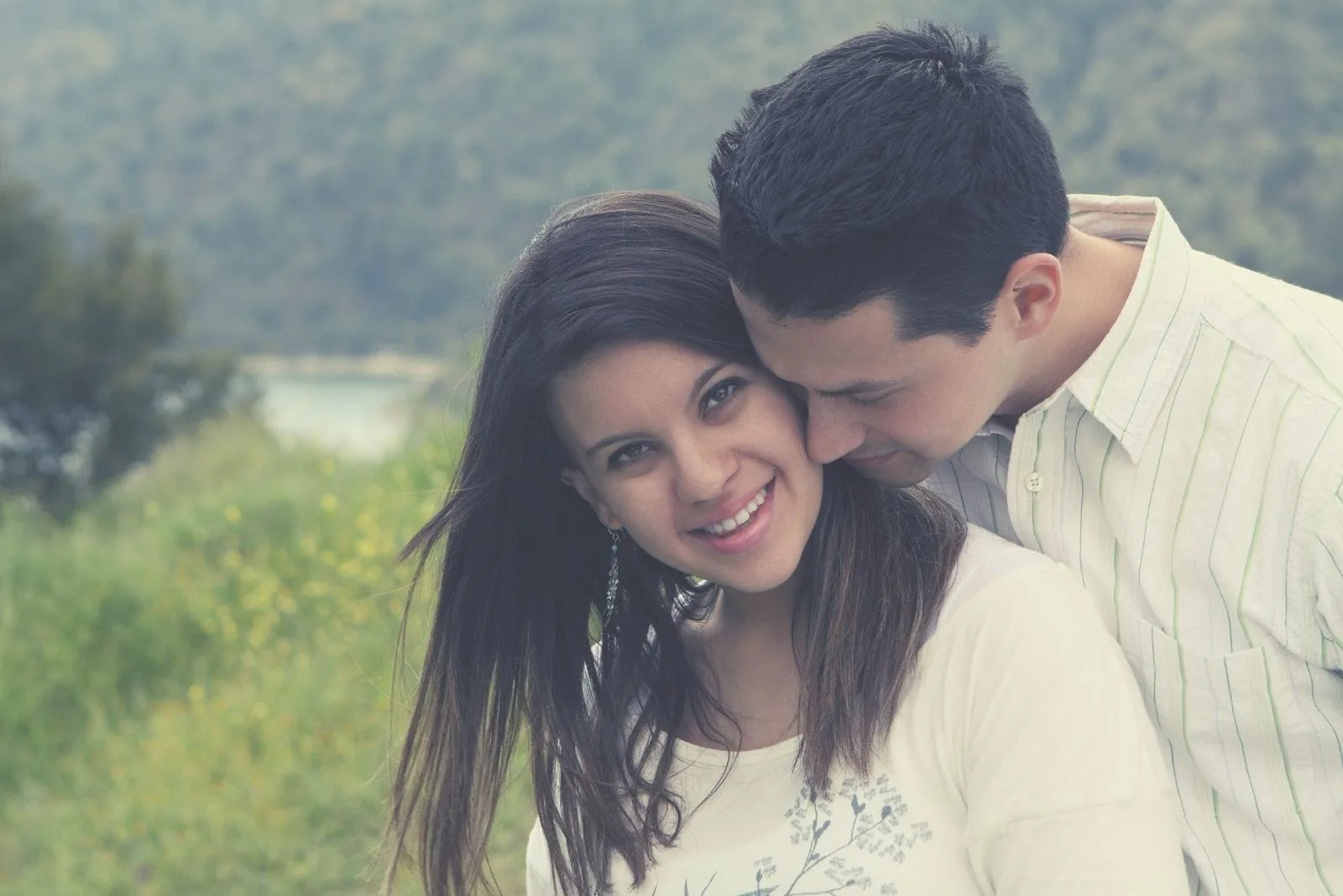 man snuggling attractive woman standing in the field in close up image