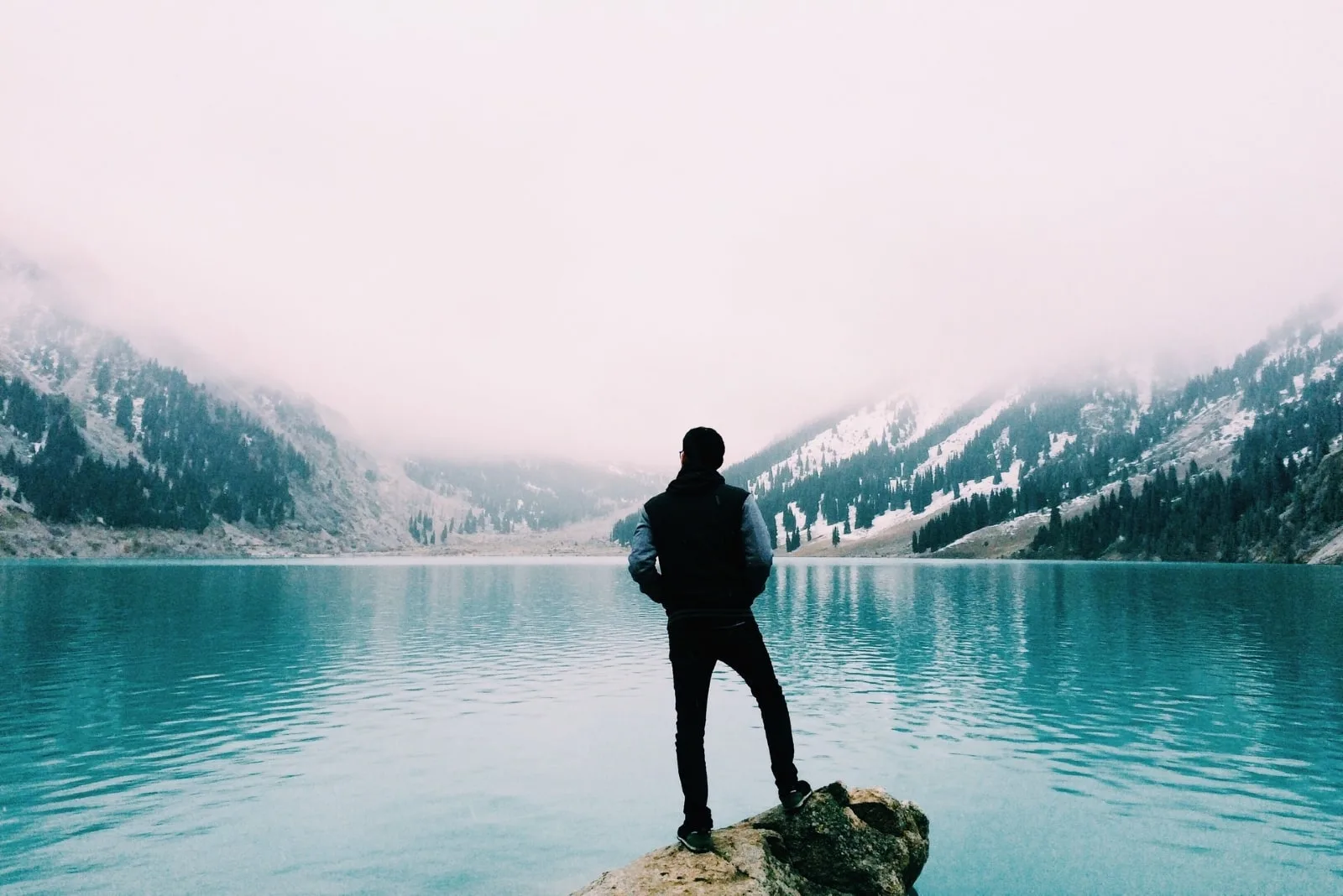 man standing on rock looking at lake