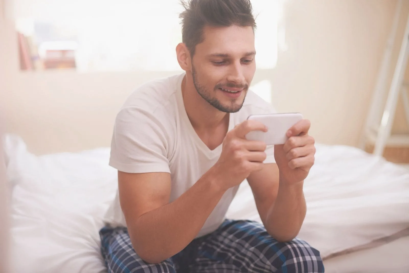 man texting up friends in bed smiling and using smartphone