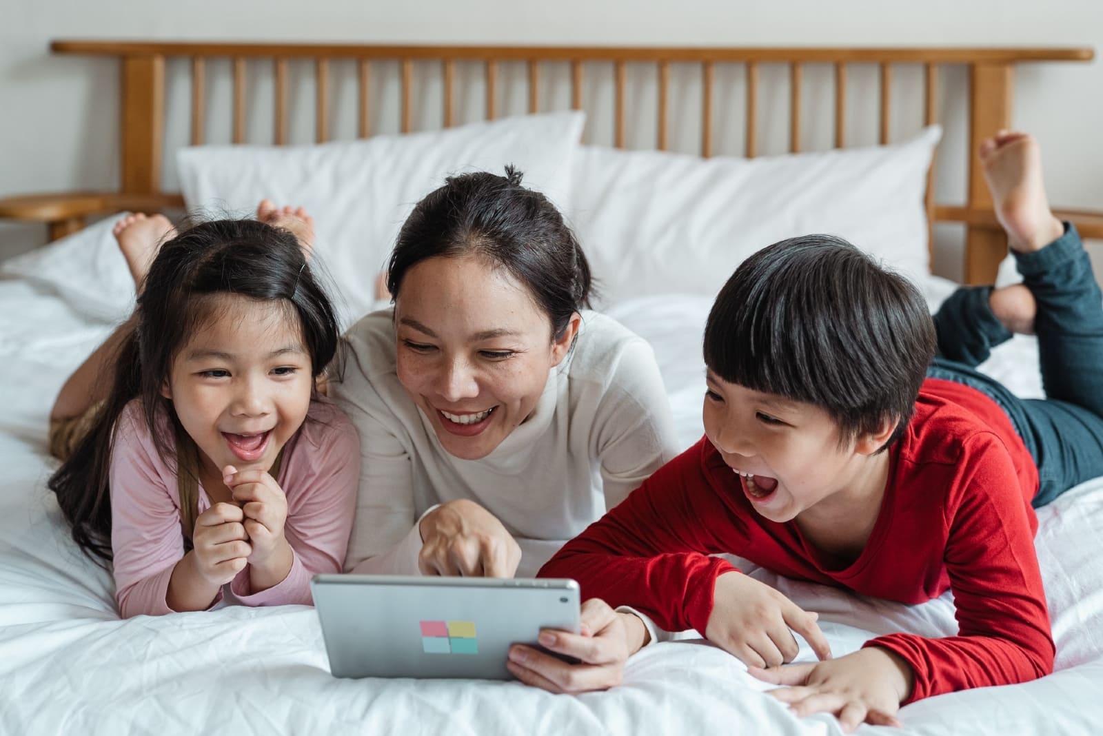 mother and children looking at tablet while laying on bed