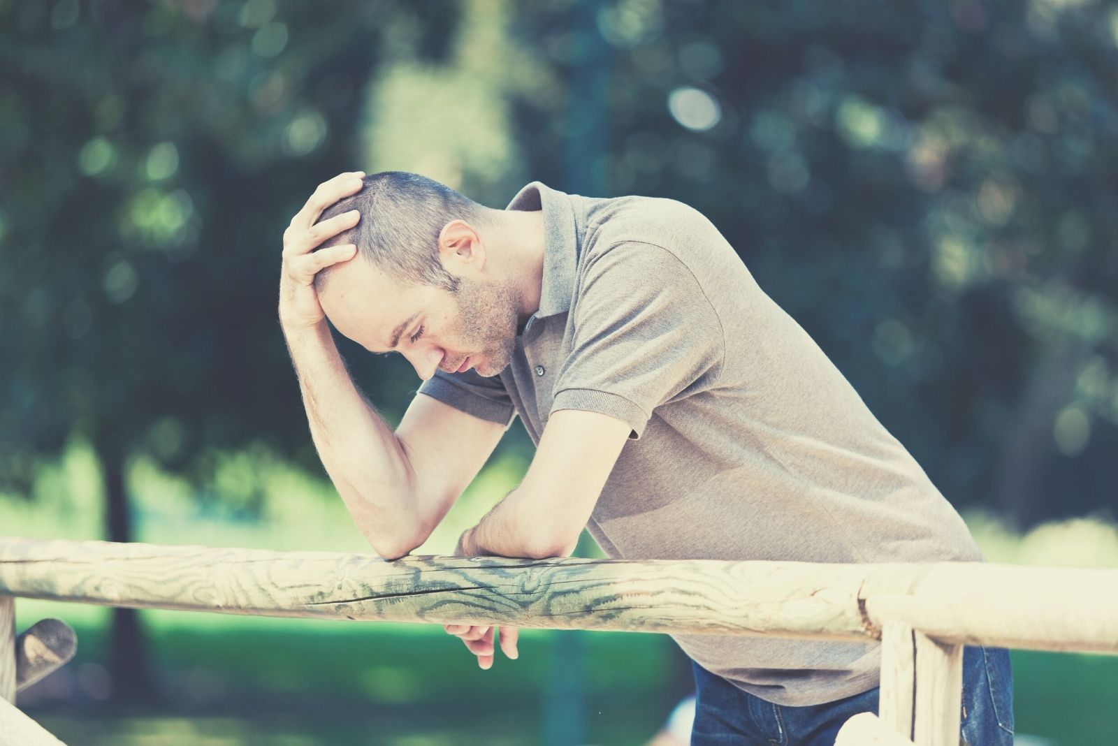 pensive semi bald man holding his head while leaning on a railing outdoors