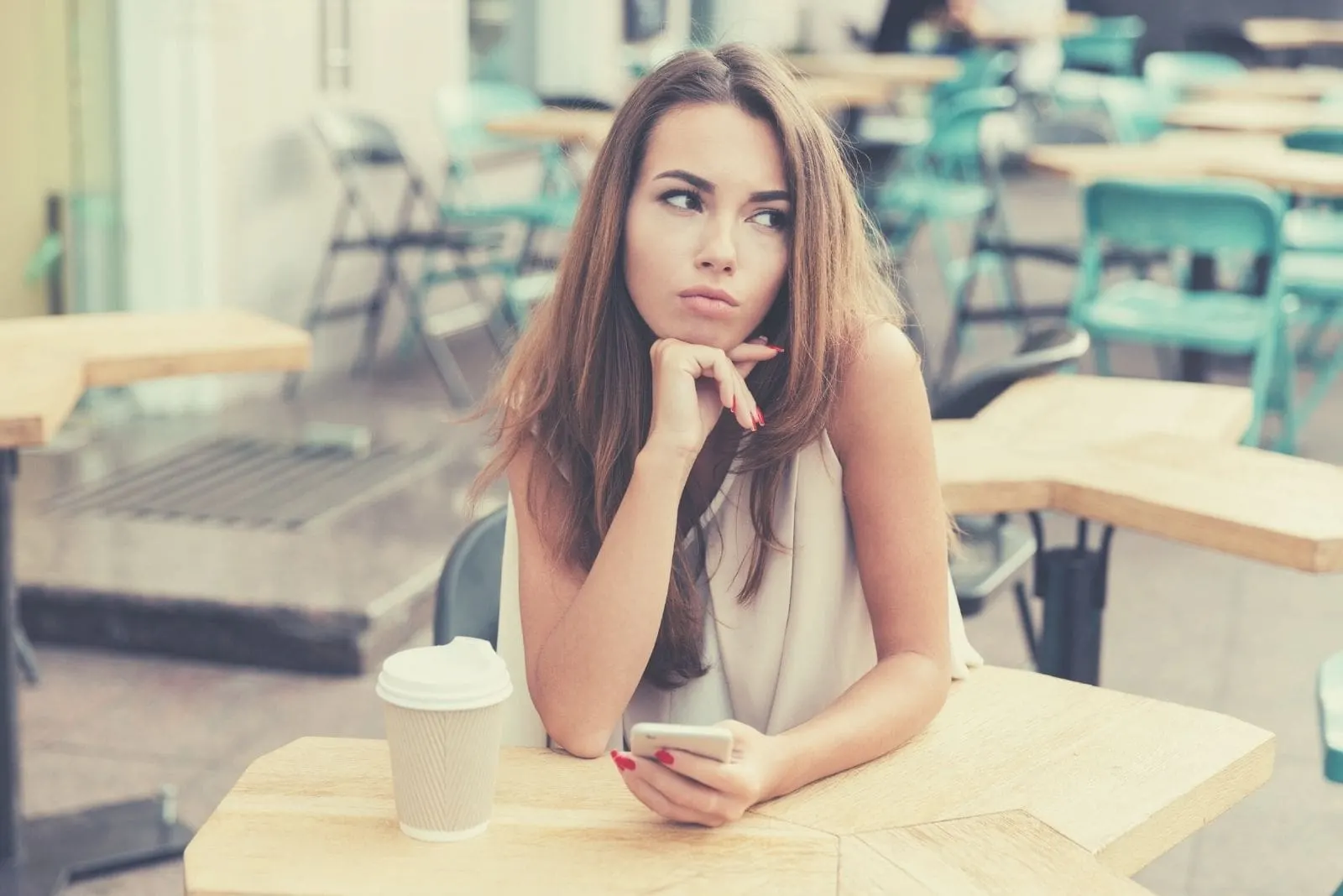 pensive woman holding a phone while sitting in the airy cafe