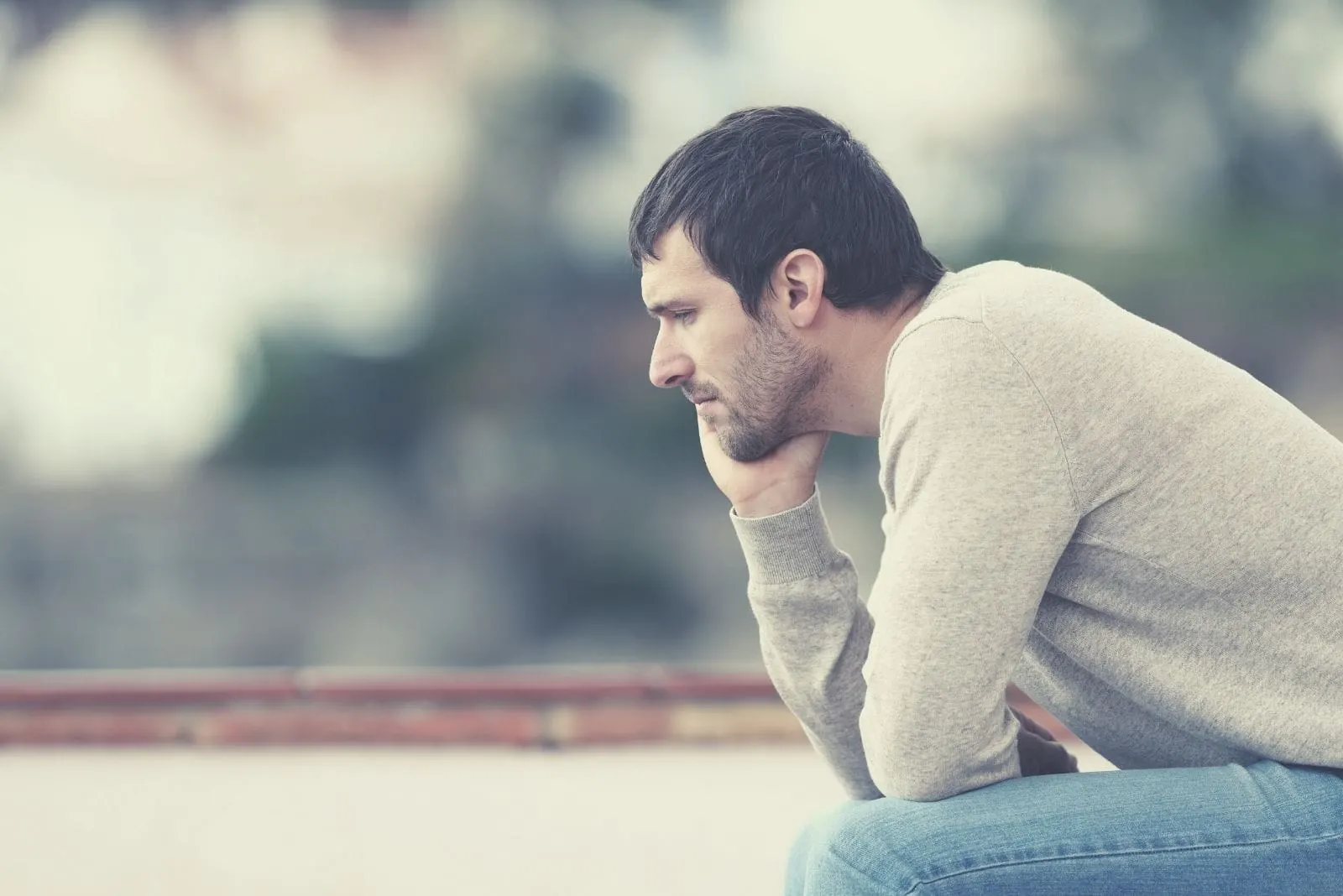 pensive worried man sitting outdoors with head leaning on his hand