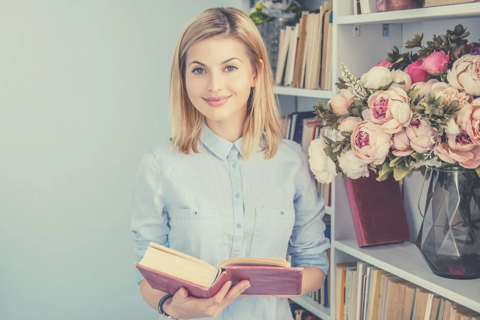 portrait of a positive woman holding a book and smiling and looking at the camera