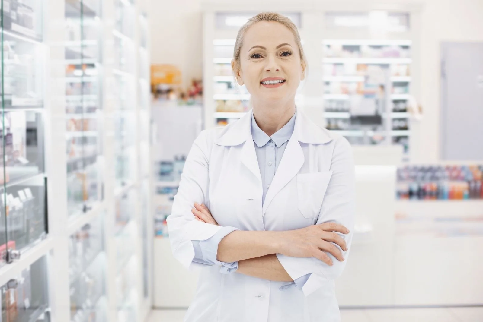 positive female pharmacist standing inside the pharmacy with arms crossed