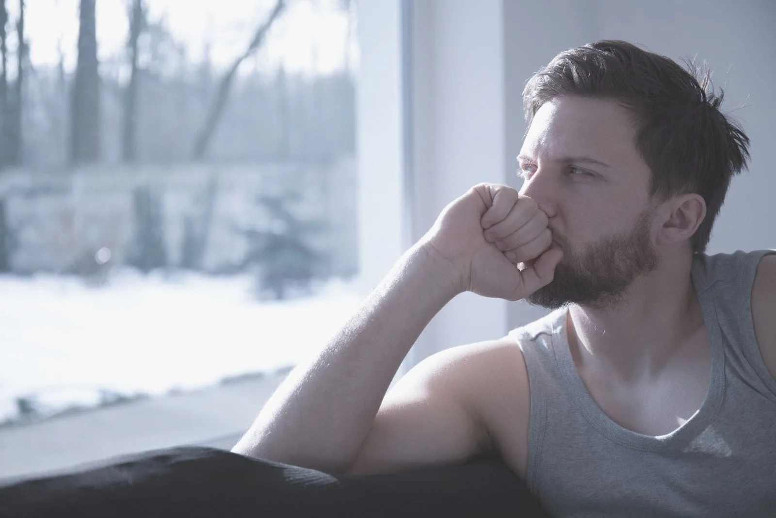 sad man deeply thinking sitting near the windows with hand on the mouth