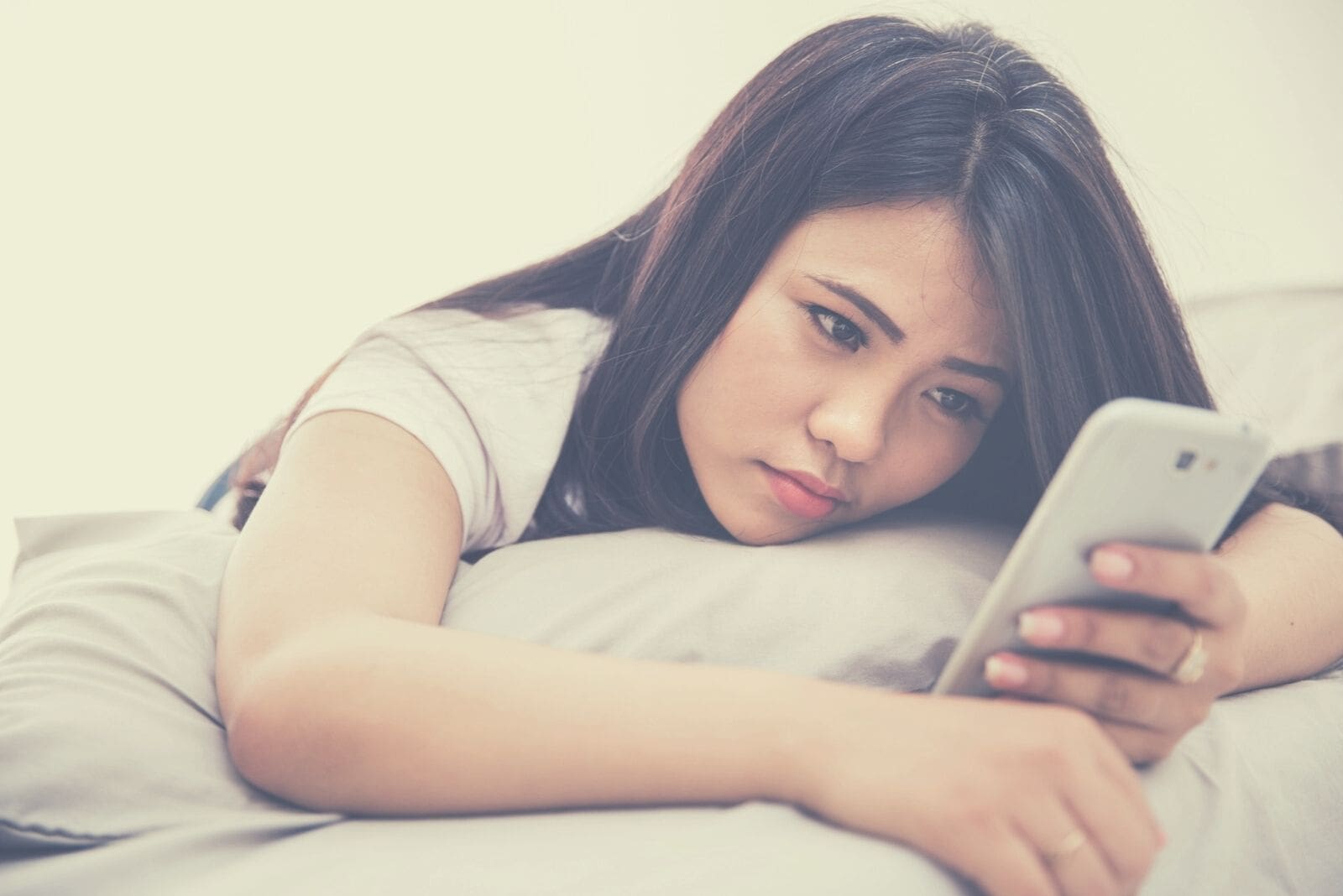 sad woman looking at phone and lying down leaning on the pillow