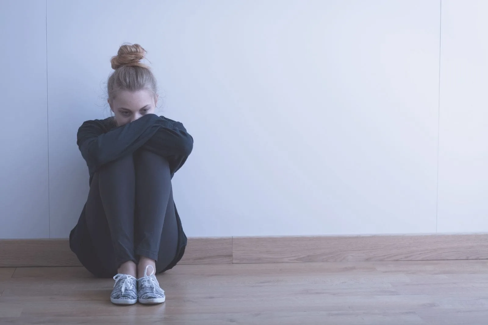 sad woman wearing black sweater and pants sitting on the floor inside an empty room