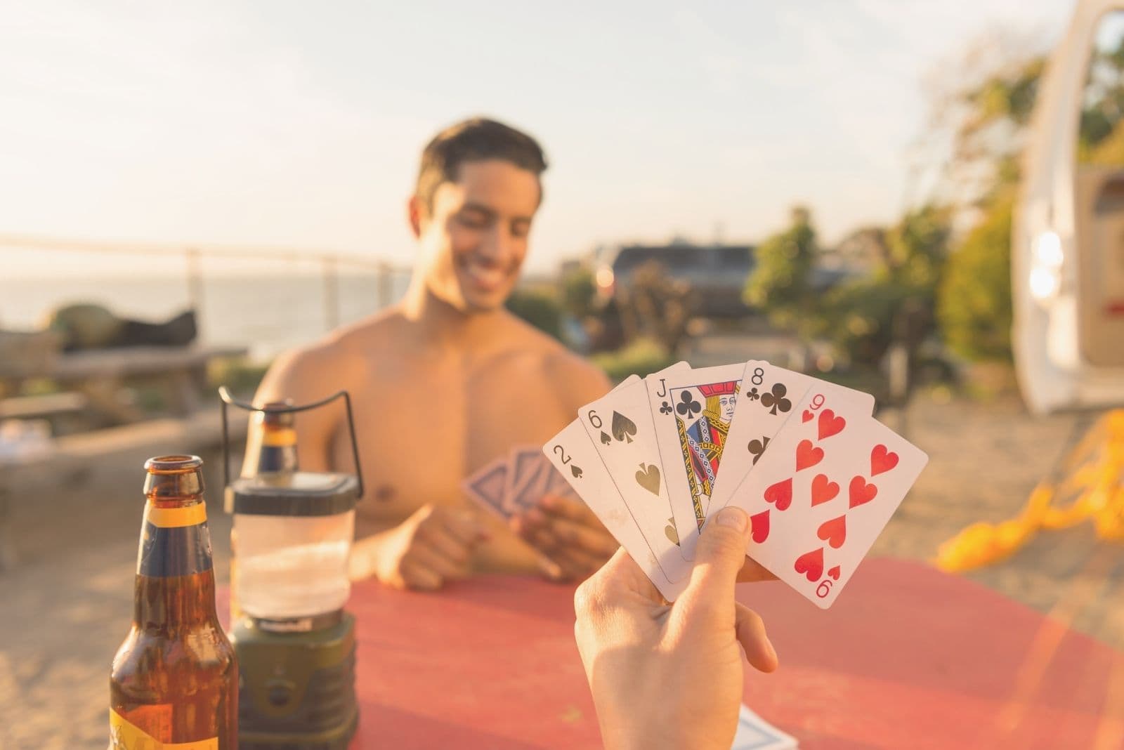 shirtless man playing cards outdoors with his girlfriend in cropped image