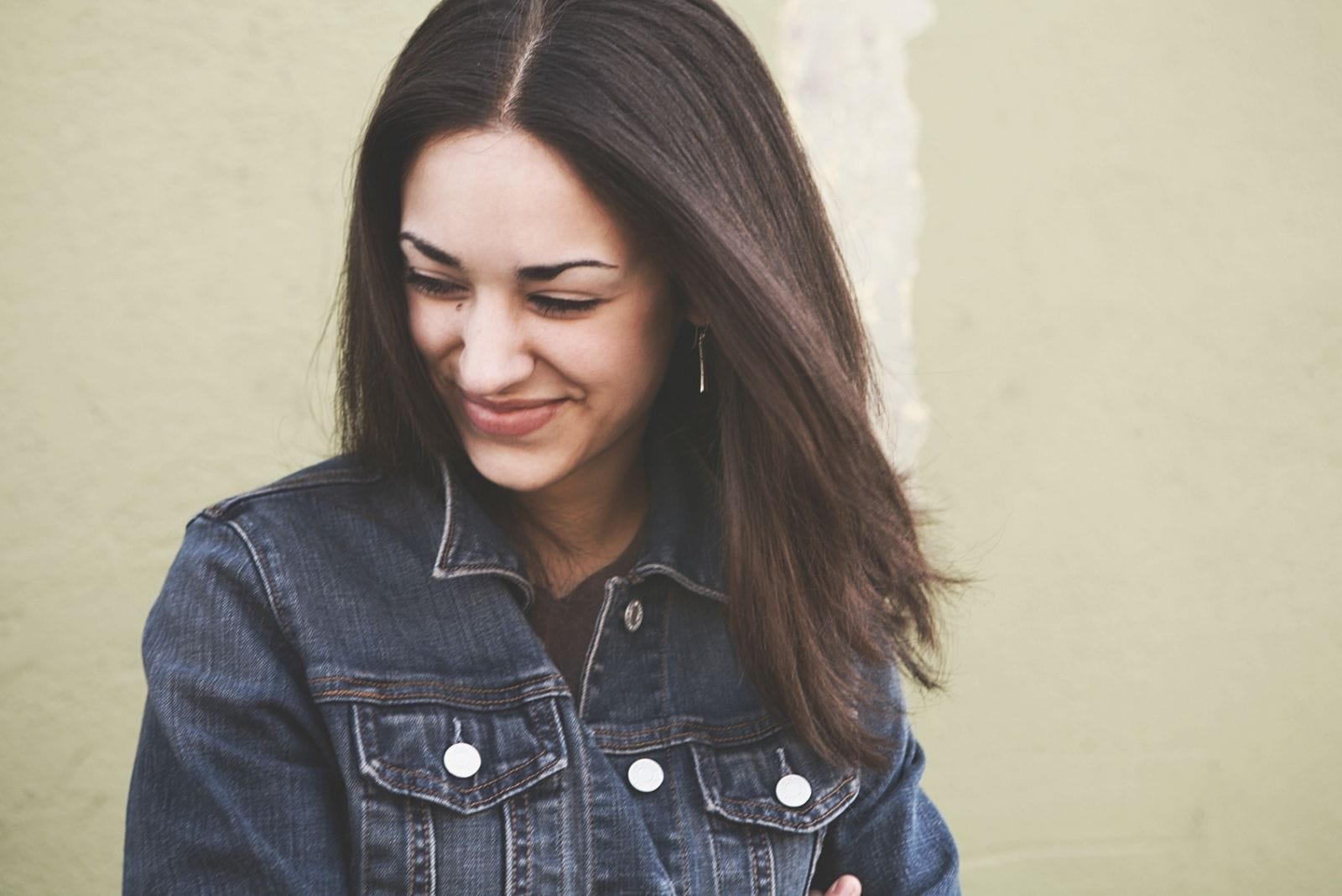 shy young woman wearing denim jacket smiling 