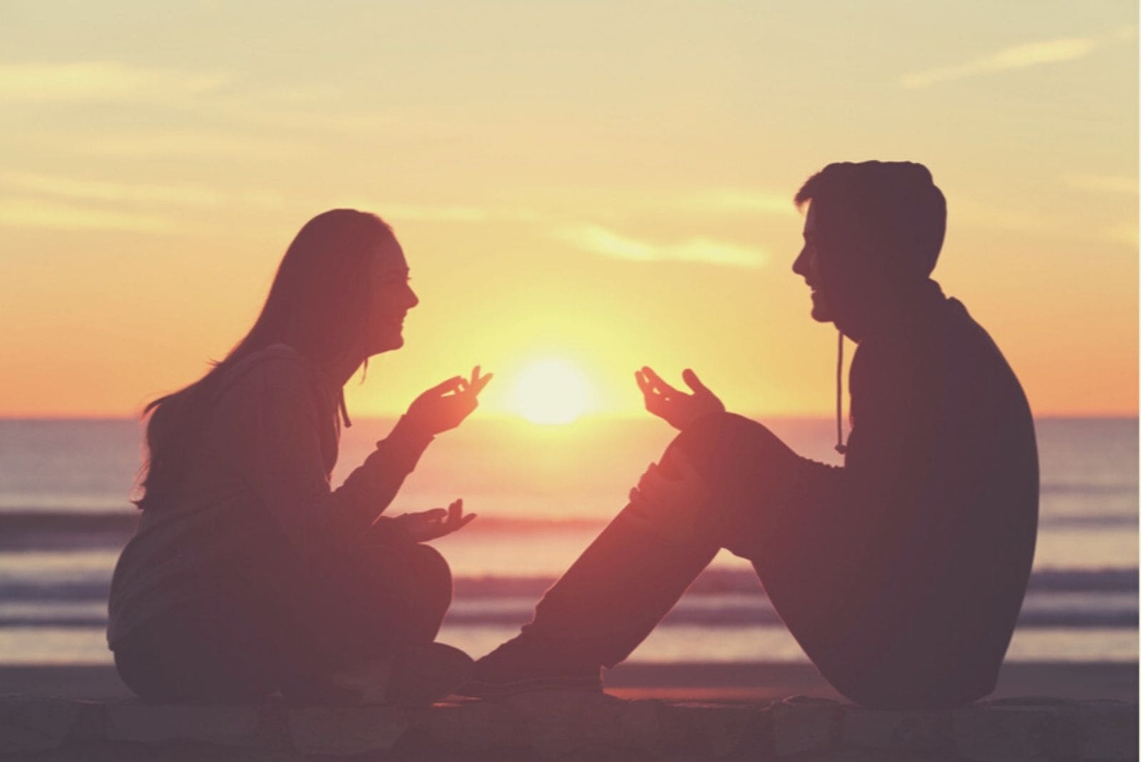 silhouette image of a couple talking to each other sitting on a breakwater during sunset