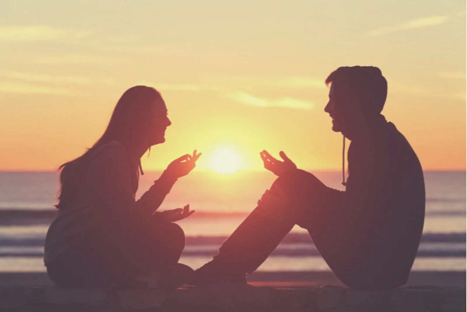 silhouette image of a couple talking to each other sitting on a breakwater during sunset